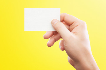 Male hand holding white business card at isolated yellow background mockup.