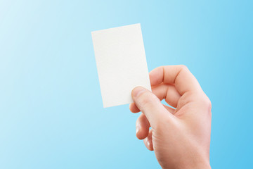 Male hand holding white business card at isolated blue background mockup.