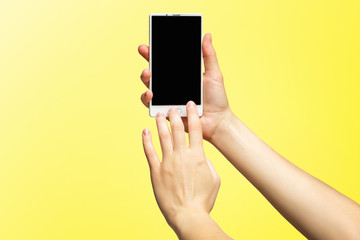 Fototapeta na wymiar Mockup of female hands holding modern white cellphone with black screen and making sliding gesture isolated at yellow background.