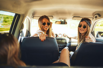 Three women enjoying road trip. They chatting while sitting in the car.