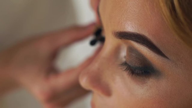 Face attractive woman while appliction mascara on eyelashes in makeup studio. Make up artist application mascara close up. Wedding makeup for happy bride.