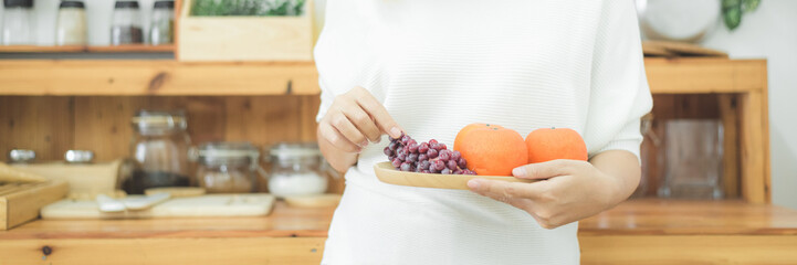Asian beautiful woman holding fruit and vegetable in the kitchen at her home. Happy pretty asian female eat freshness fruit for healthy body. lifestyle asia woman at home concept. Panoramic banner.