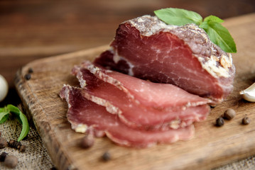 Pork dried meat slices on rustic dark wooden background. Dried pork prosciutto salami ham with herbs.