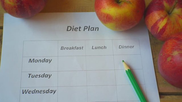 Diet Plan.Ripe apples blank food schedule and pencil lie on a wooden table.View from above.Closeup