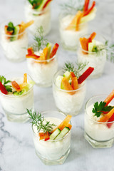 Snack in a glass with fresh cream and various vegetables on a light background.