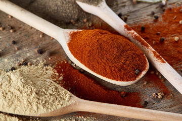 Top view of a wooden spoons full of paprica and black pepper on wooden barrel background, selective focus.