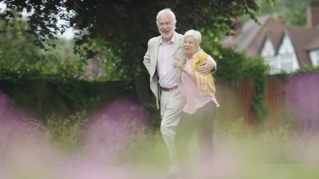 Senior retired couple walking hand in hand through  garden 