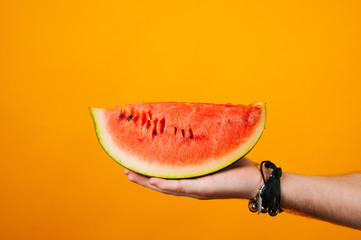 Hand of a man holding a great slice of watermelon on yellow background.