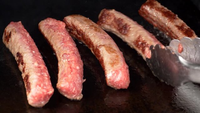 UHD shot of the delicious meat sausages frying on the iron