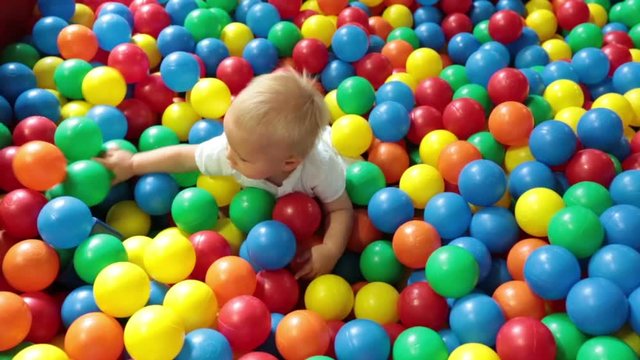 Cute toddler boy, child, playing in colorful balls in children playground, indoors