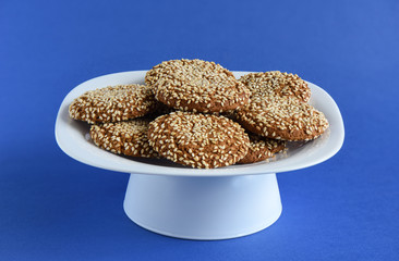 Oatmeal cookies with sesame seeds in a white dish on a violet ba