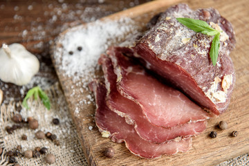 Pork dried meat slices on rustic dark wooden background. Dried pork prosciutto salami ham with...