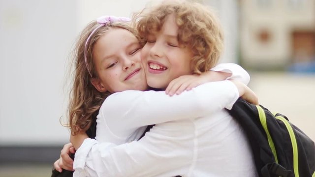 Schoolchildren embrace after the summer holidays. again to school. Day of knowledge. Lovely children, boy and girl hug each other, smile, schoolchildren are dressed in white shirts
