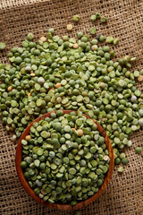 Organic green peas in a bowl on burlap tablecloth, close-up, top view, selective focus.