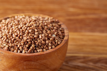 Bowl full of buckwheat grains on rustic wooden table, close-up, selective focus, shallow depth of field.