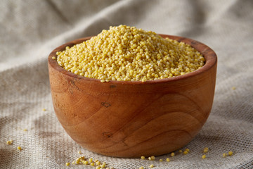 Millet in a wooden bowl on homespun tablecloth, top view, close-up, selective focus.