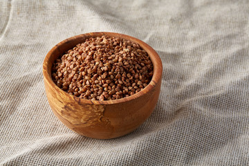 Flax seeds in a wooden plate on homespun tablecloth, top view, close-up.