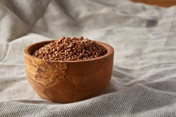 Flax seeds in a wooden plate on homespun tablecloth, top view, close-up.