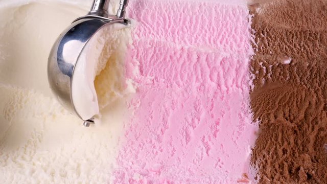 Vanilla strawberry chocolate ice cream scooped out from container with a spoon. Closeup 4k