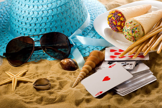 image of hat, sunglasses, ice cream,sea shells, cards and books on the sand