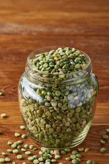 Raw green peas in glass jar over wooden background, close-up, selective focus.