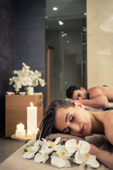 Young couple relaxing under the stimulating effects of a traditional hot stone massage at luxury...