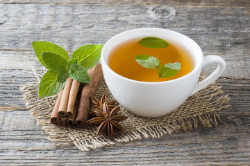 Cup of tea with fresh mint leaves and cinnamon anise on a wooden background. Copy space