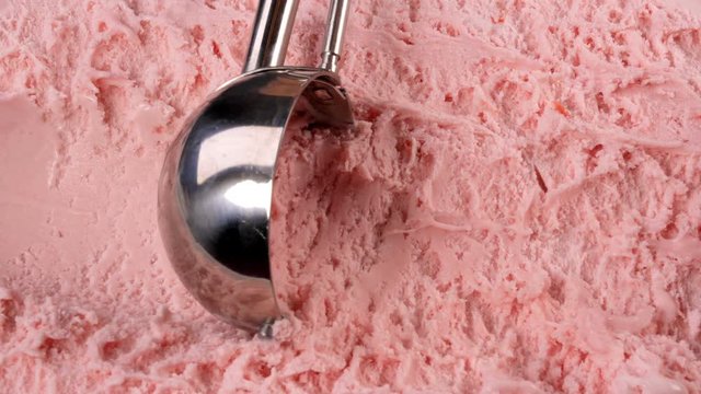 Strawberry ice cream scooped out of container with a utensil. Closeup 4k