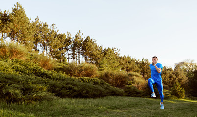 Image of young fit male runner exercising on green grass in the park. Horizontal shot of handosme athlete running and sprinting outdoor preparing for marathon. Sport and people concept.
