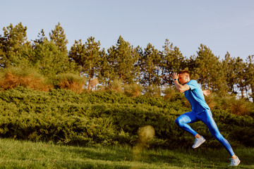 Side view of fit young male jogger exercising on green grass in the park. Handosme athlete running...