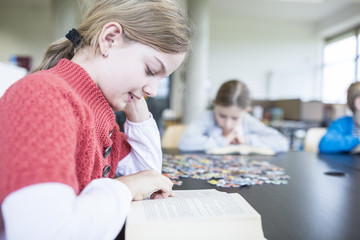 Fototapeta na wymiar Schoolgirl reading book on table in school break room