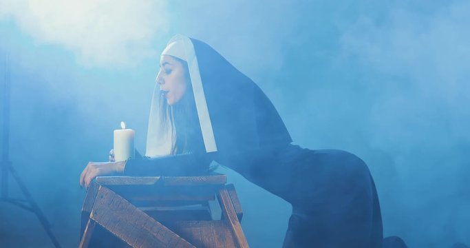 Attractive sexy nun blows out a candle in a dark smoky studio