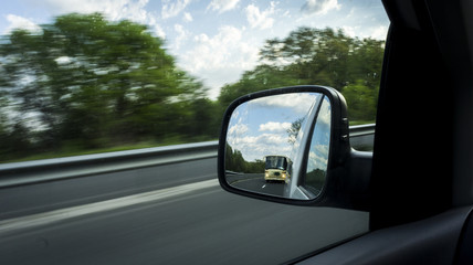 reflection of a car mirror that shows a bus that drives fast.scene from a moving motorway on a...