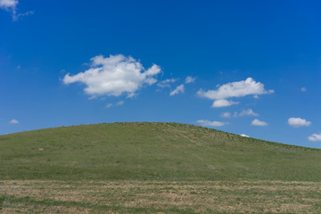 Green hill covered with grass against a blue sky with clouds.