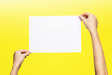 Mockup of female hands holding blank paper list isolated at yellow background.