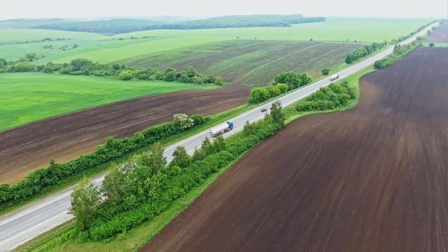 Aerial view of straight countryside road with cars amidst beautiful freshly plowed fields and growing plants on summer day
