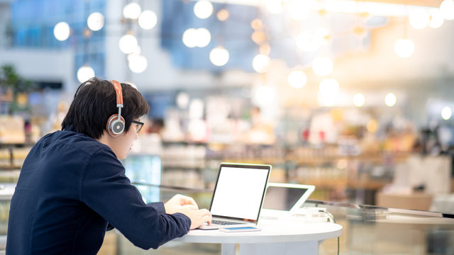 Young Asian business man listening to music by headphones while working with laptop computer in co working space. freelance or digital nomad lifestyle in urban workspace concepts