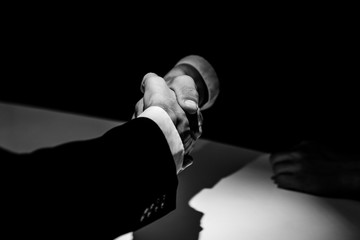 Anonymous business partners making handshake in shadow - obrazy, fototapety, plakaty