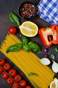 Italian food background. Ingredients for cooking pasta: spaghetti, tomato, basil and pepper on a dark concrete background.