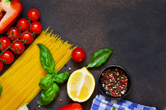Italian food background. Ingredients for cooking pasta: spaghetti, tomato, basil and pepper on a dark concrete background.