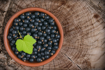 Berries of black currant in a brown ceramic bowl on a wooden background with cracks