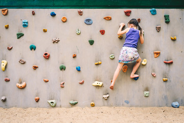 little girl climbing a rock wall outdoor at children playground - 211002828