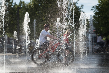 boy rides his bike among fountains in summer day