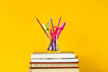 A glass with pens, pencils and scissors on a pile of books for training. Back to school concept. On...