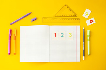 Notebook in the cell among pens, pencils, numbers and rulers on a yellow background. Accessories...