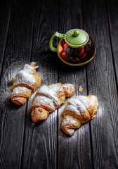 three croissants with tea on dark wooden background close-up top view