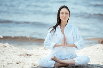 Concentrated young Asian woman in anjali mudra (salutation seal) pose on beach