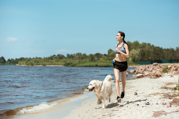 young asian sportswoman running with golden retriever on beach