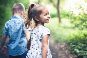 Happy kids walking outdoor at park hold their hands.