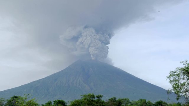 Breathtaking view of explosive eruption of Agung volcano in Bali, Indonesia: smoke and ash plume rising from crater on the peak